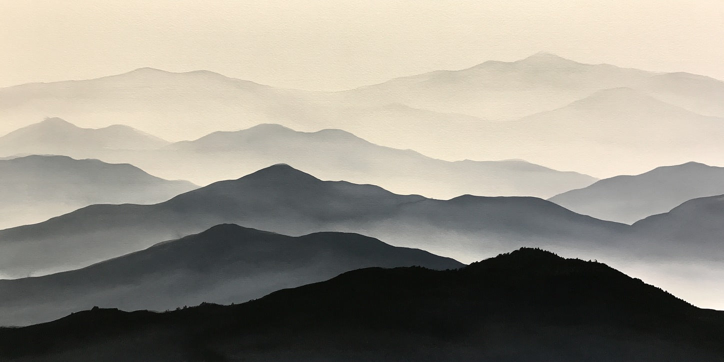 Layered black and gray mountain ridges fading into pale mist and a light sky
