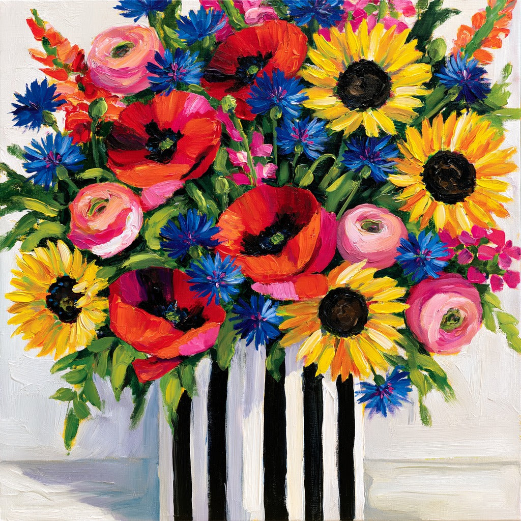 Dense wildflower bouquet with red poppies, yellow sunflowers, pink blooms, and blue flowers in a white vase