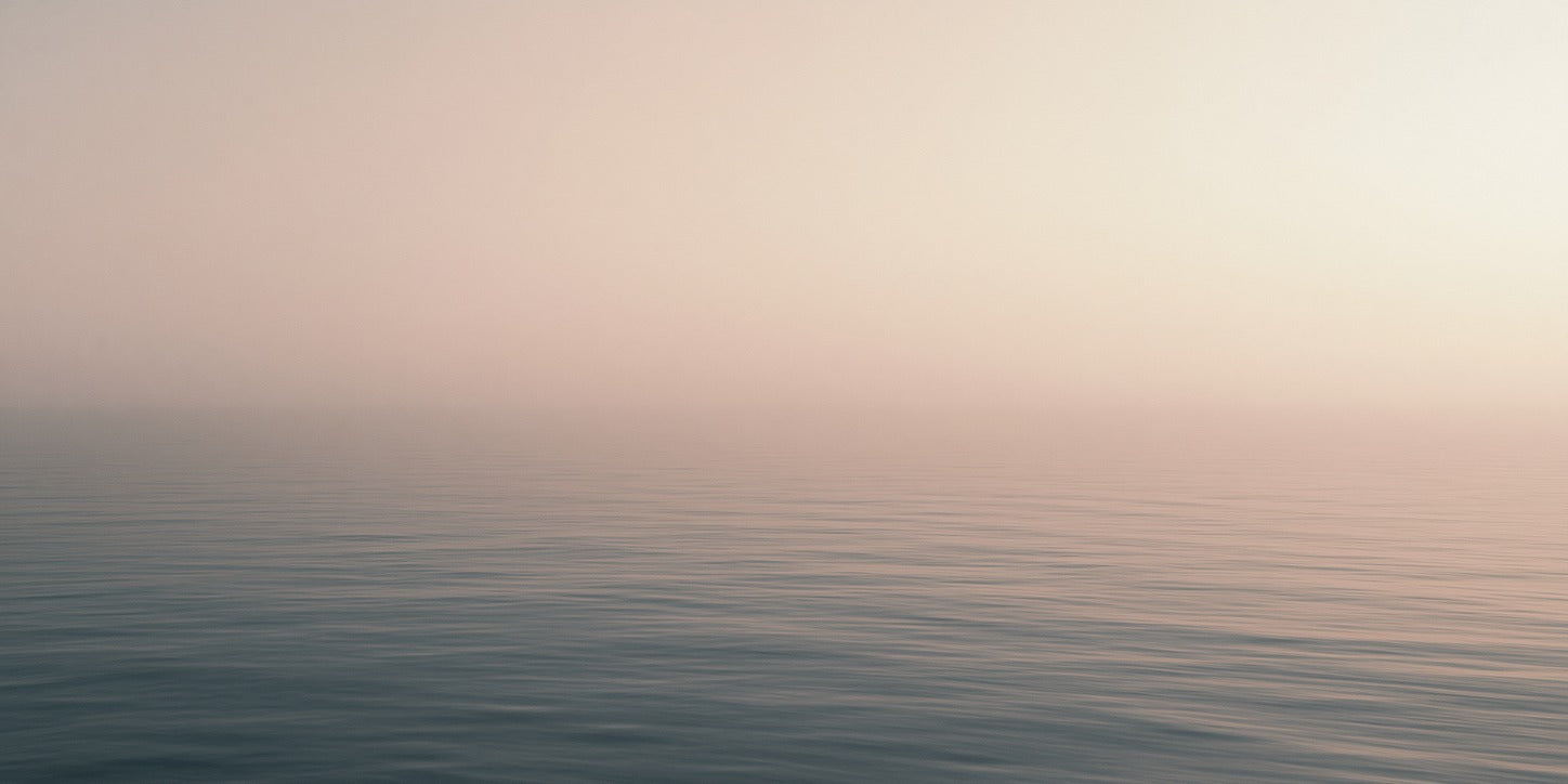 Soft blush sky over a calm blue sea with fine horizontal ripples and a low horizon