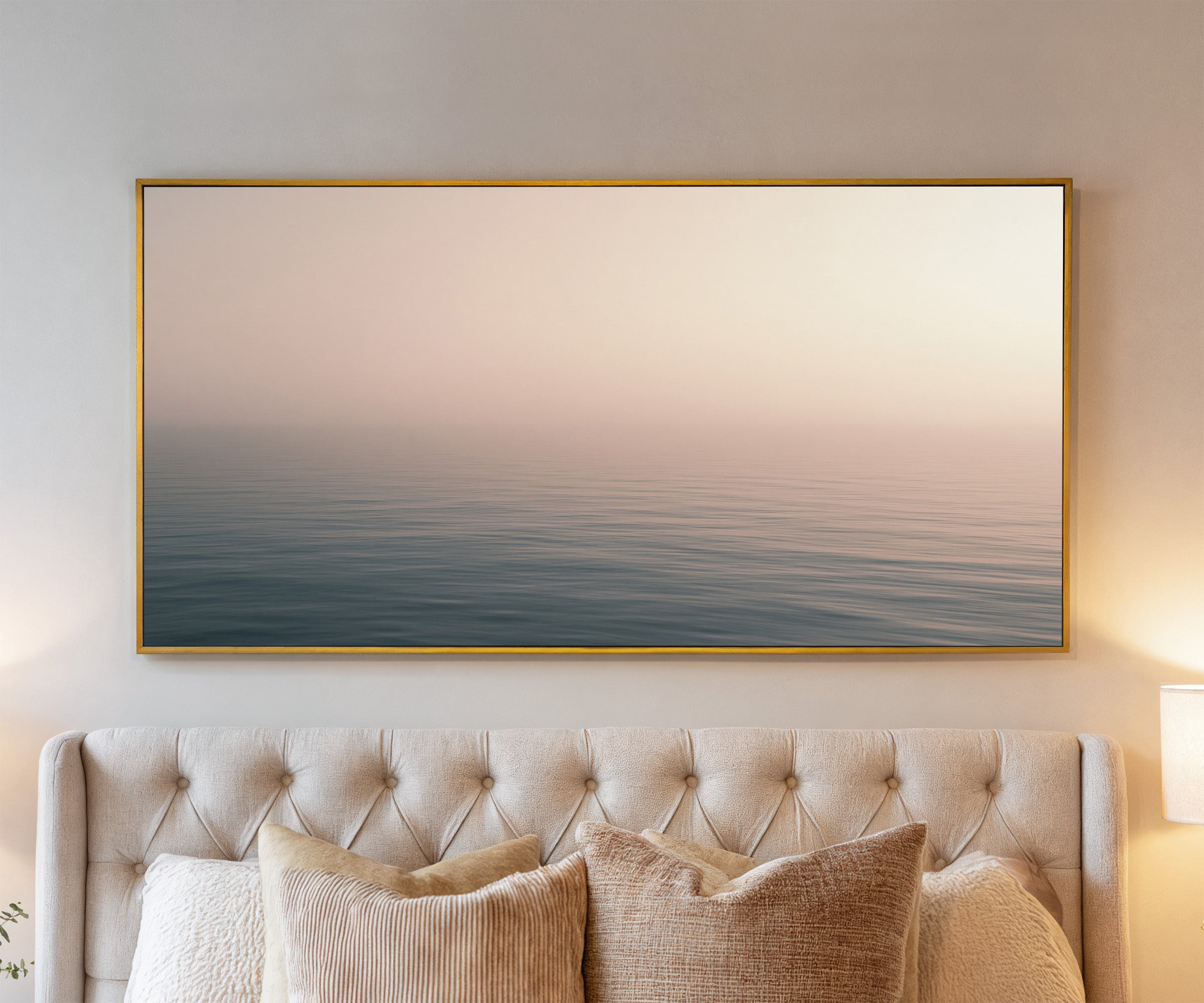soft blush and blue seascape canvas wall art in a gold frame above a bed