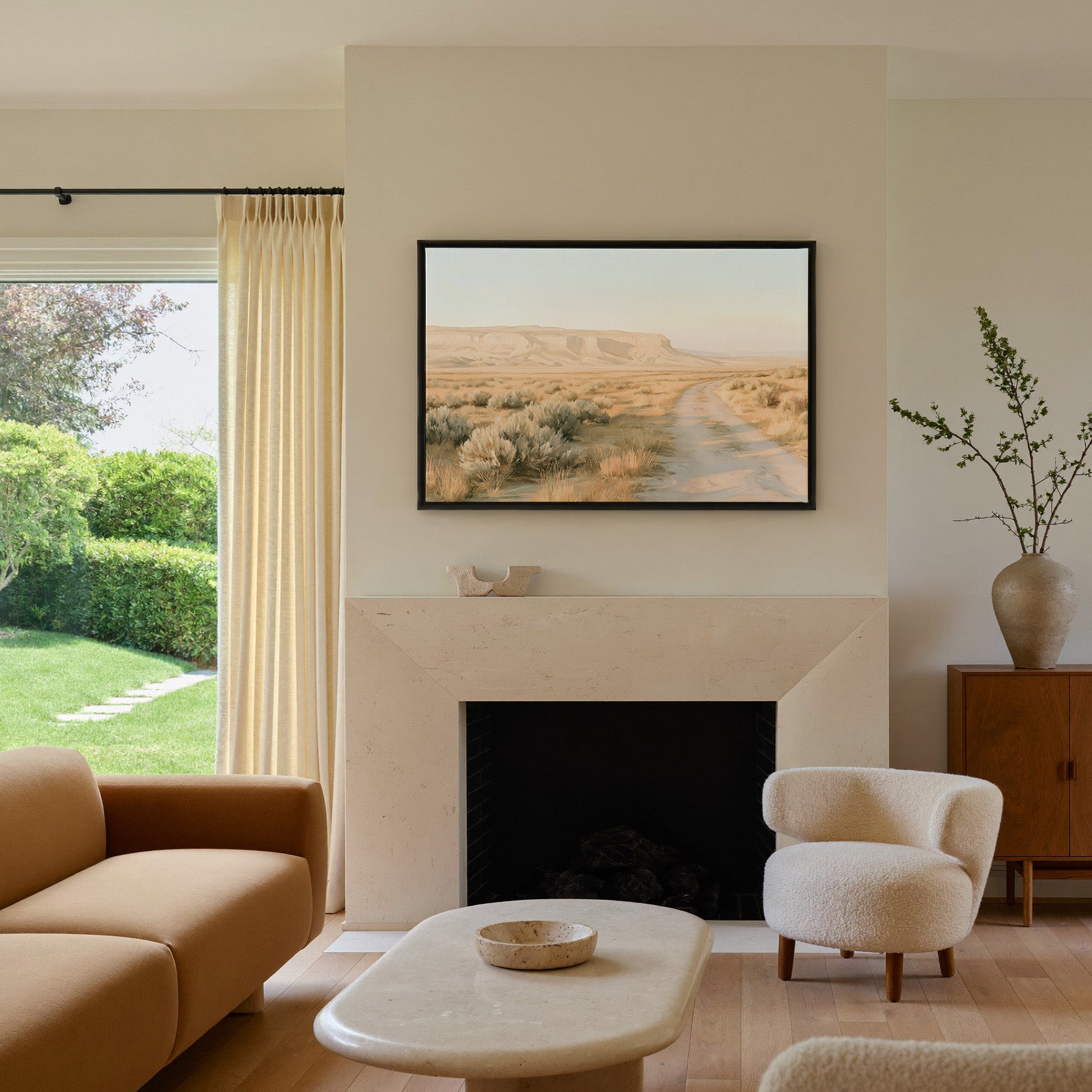 pale desert valley with a winding track and low canvas wall art in a black frame above a mantel