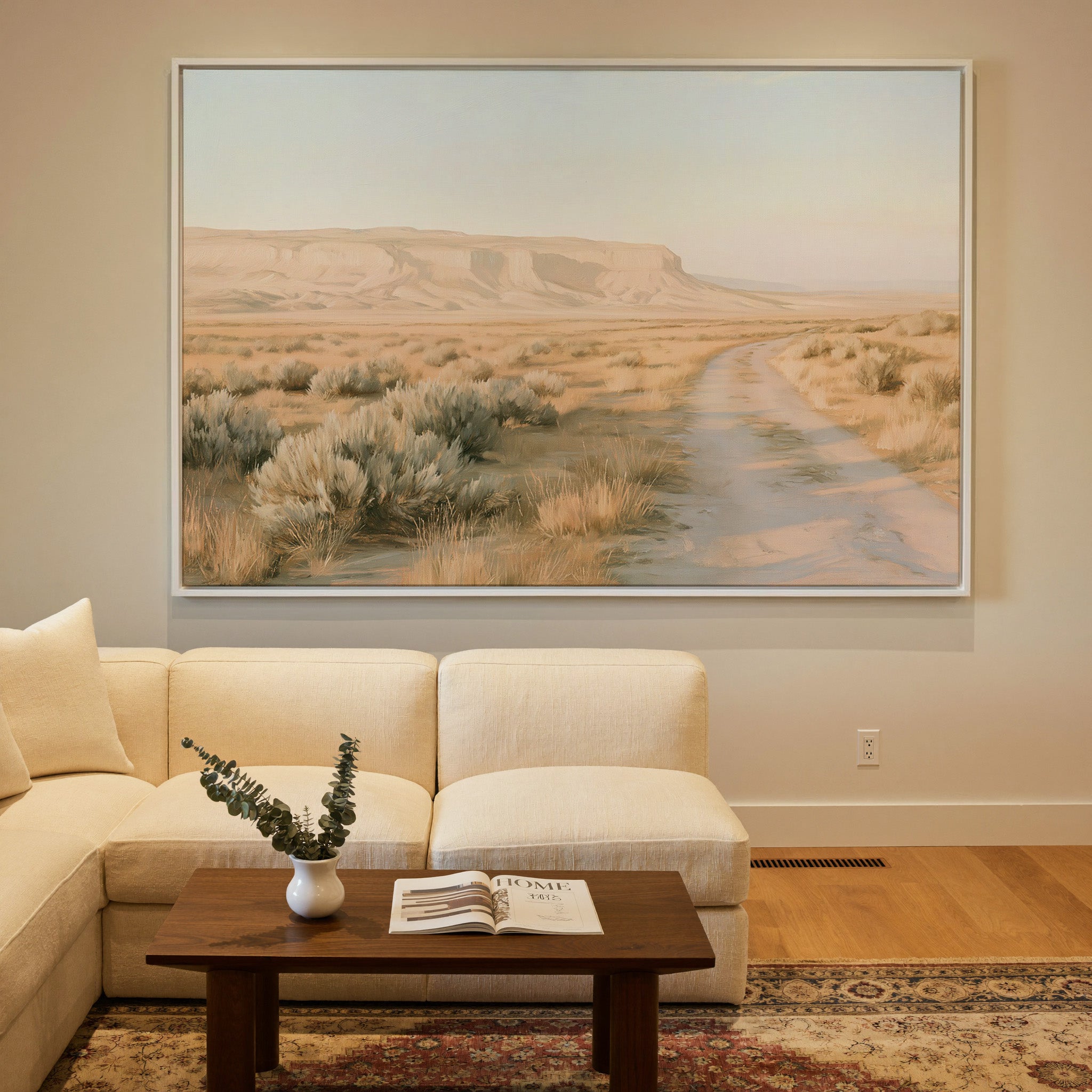 pale desert valley with a winding track and low canvas wall art in a white frame in a styled room setting