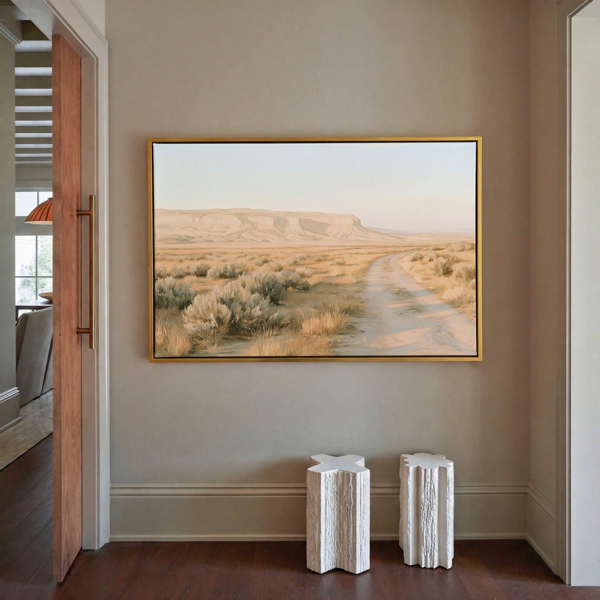 pale desert valley with a winding track and low canvas wall art in a gold frame in a styled room setting