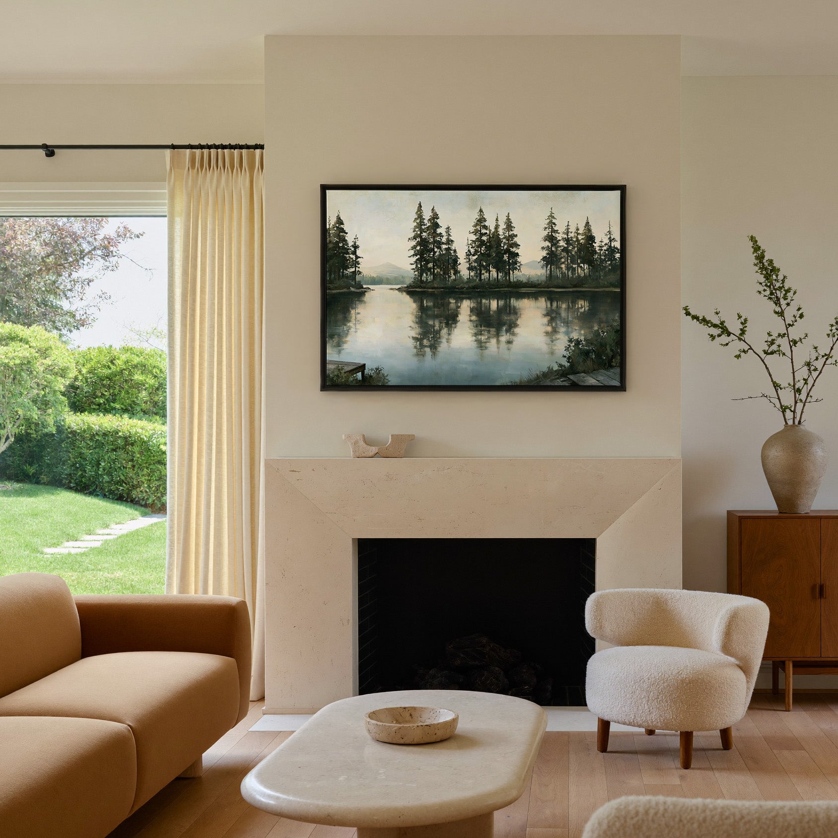 quiet lake with tall pines and pale distant canvas wall art in a black frame above a mantel