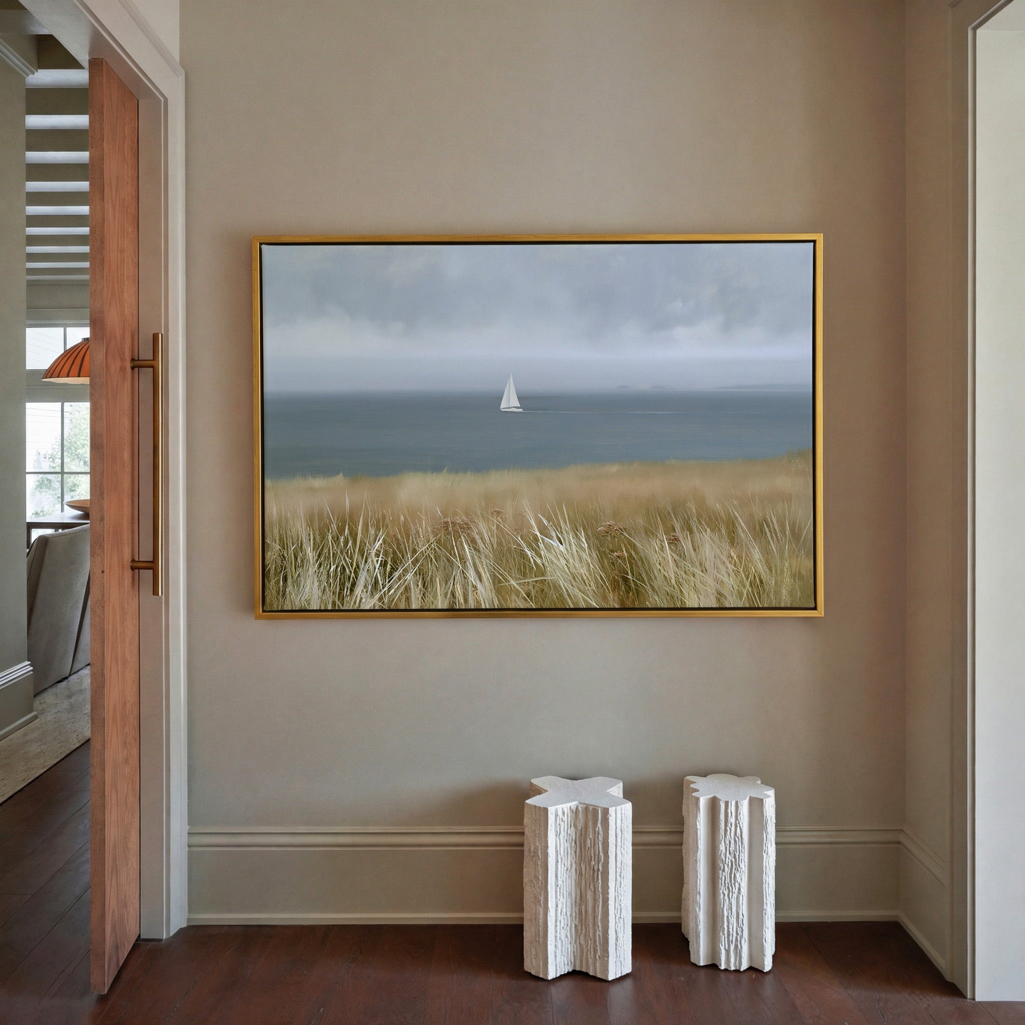 distant white sailboat on a gray blue sea canvas wall art in a gold frame in a styled room setting