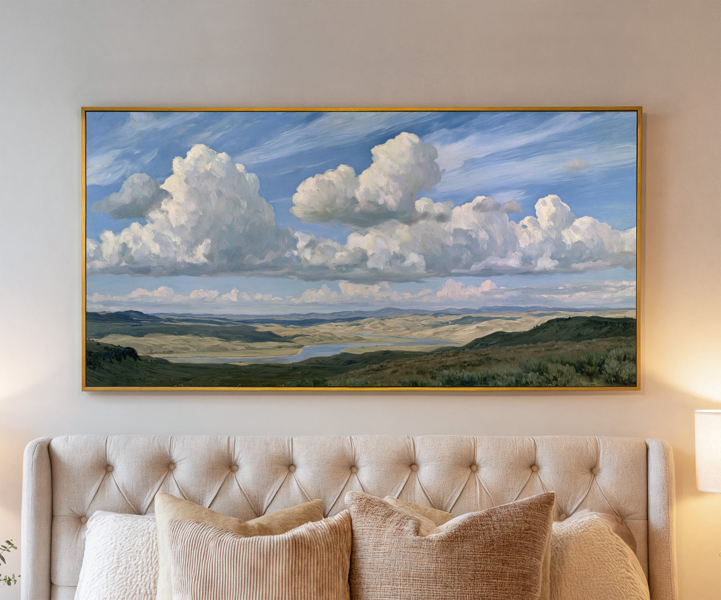 blue sky with towering white cloud banks over a canvas wall art in a gold frame above a bed