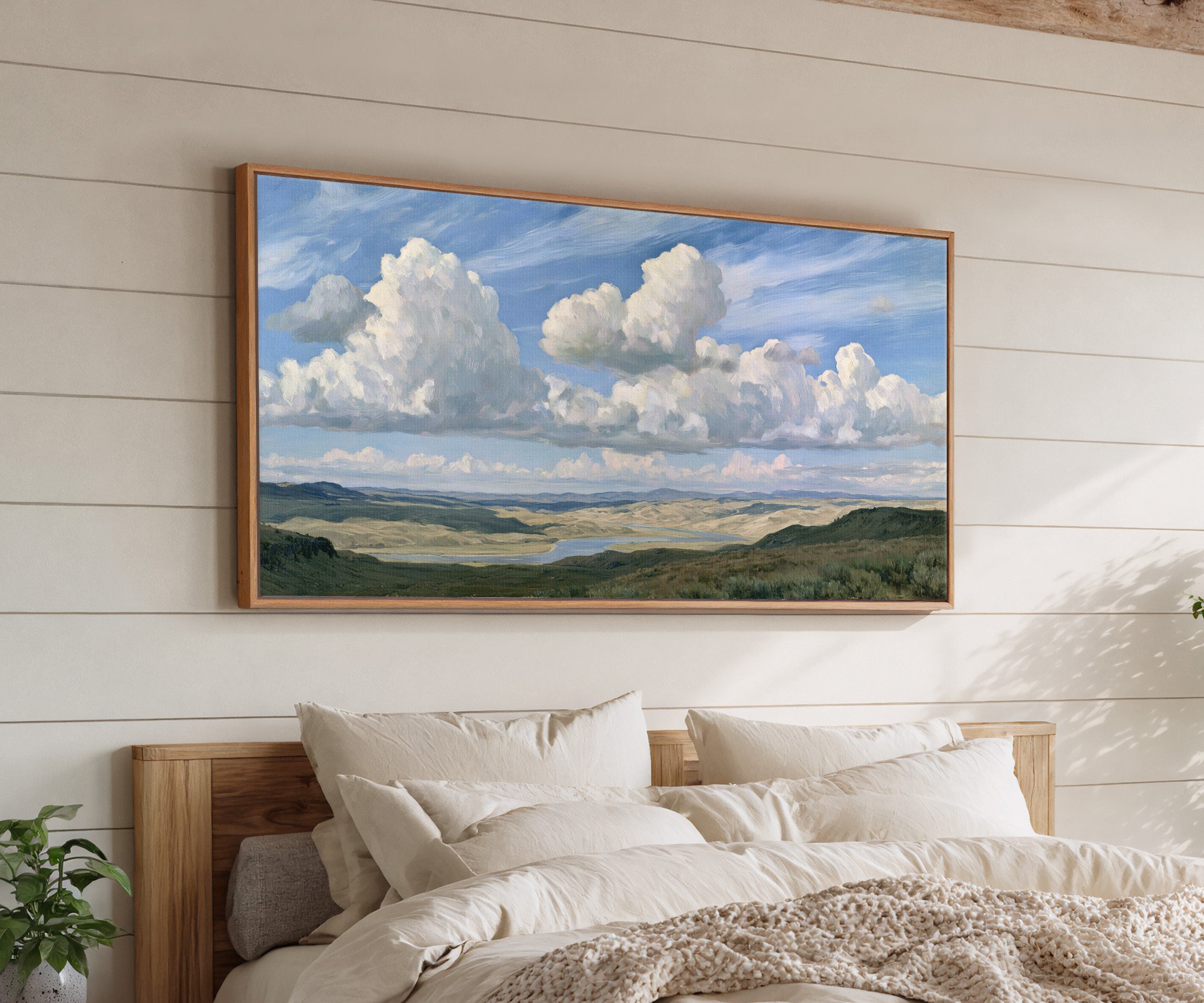 blue sky with towering white cloud banks over a canvas wall art in an oak frame above a bed