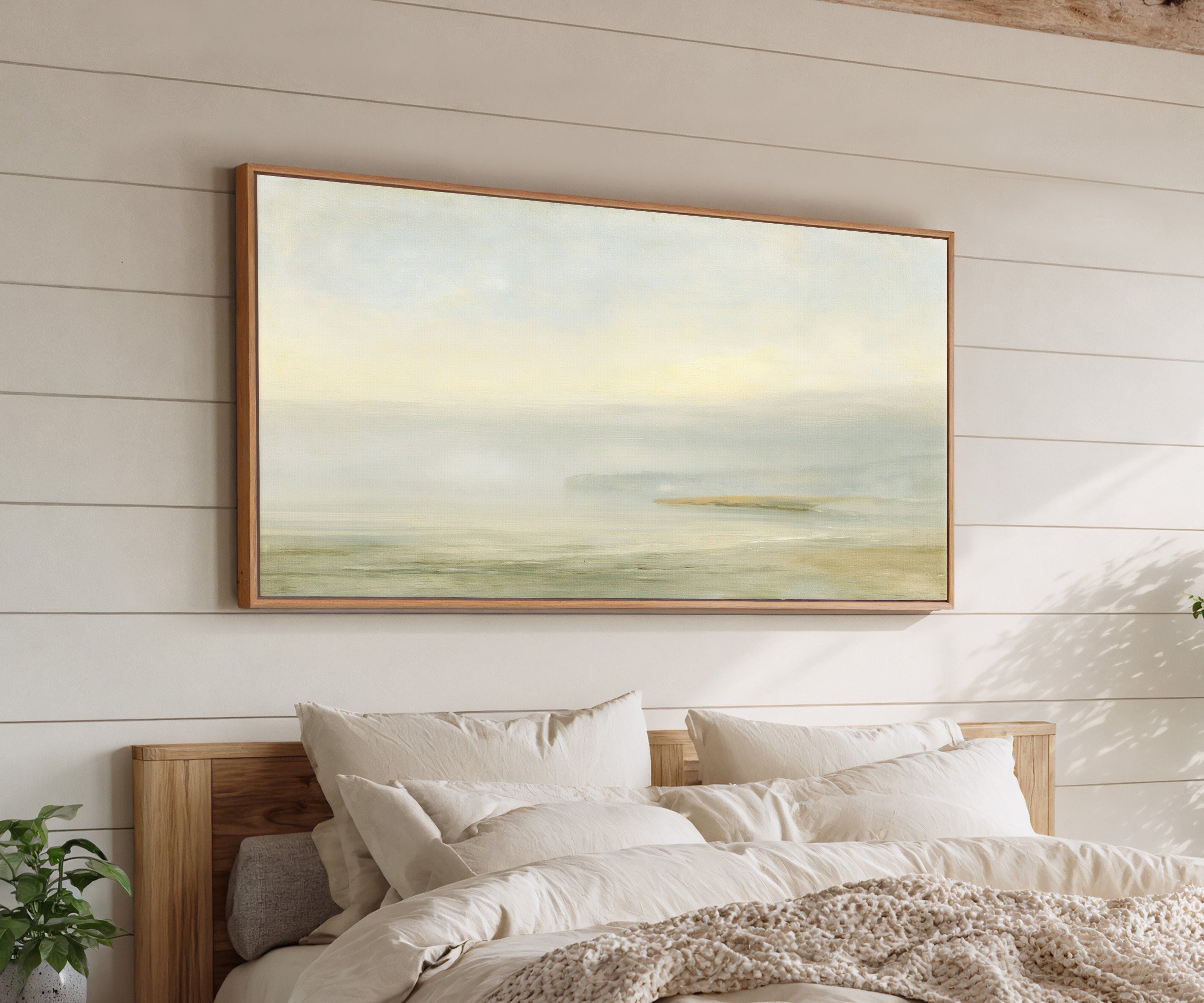 pale sea with a faint distant headland canvas wall art in an oak frame above a bed