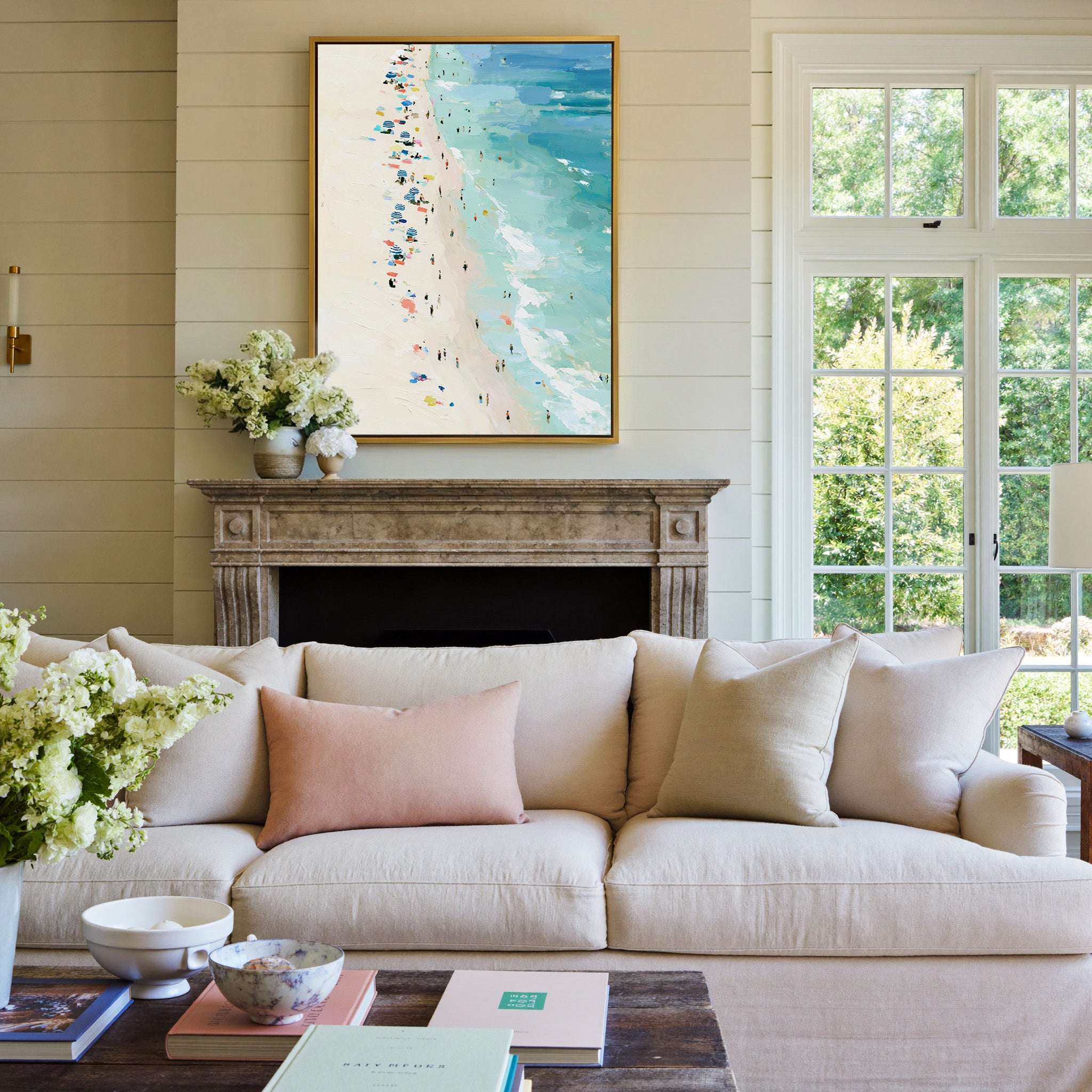 sunlit beach with turquoise water and scattered canvas wall art in a gold frame above a mantel
