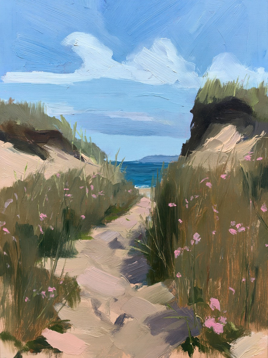 Sandy dune path between tall grass and pink wildflowers opening to blue water and sky