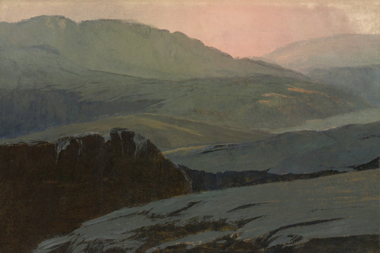 Dark foreground cliffs and layered blue green mountain ridges under a pale pink sky