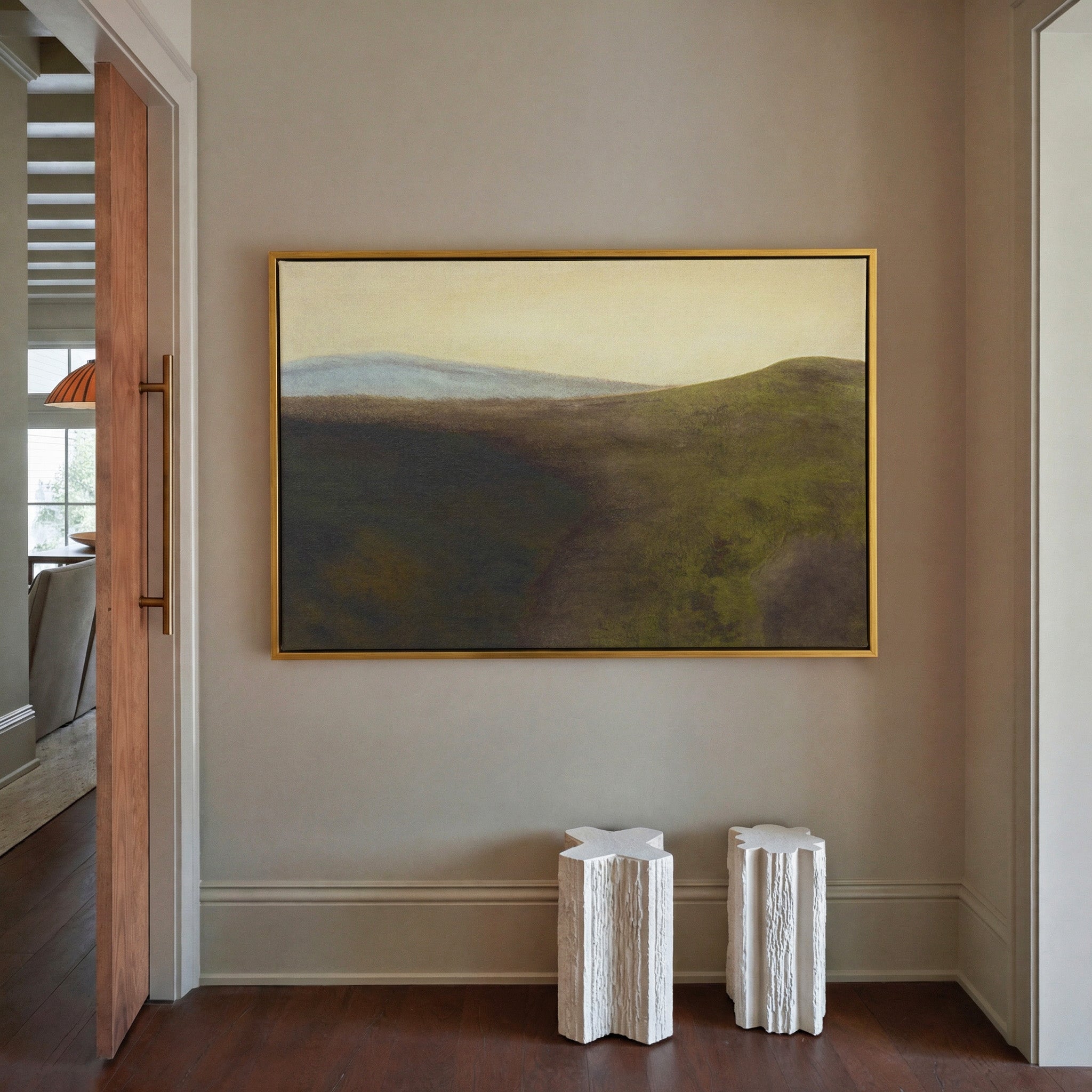 muted green hills with a pale blue ridge and canvas wall art in a gold frame in a styled room setting