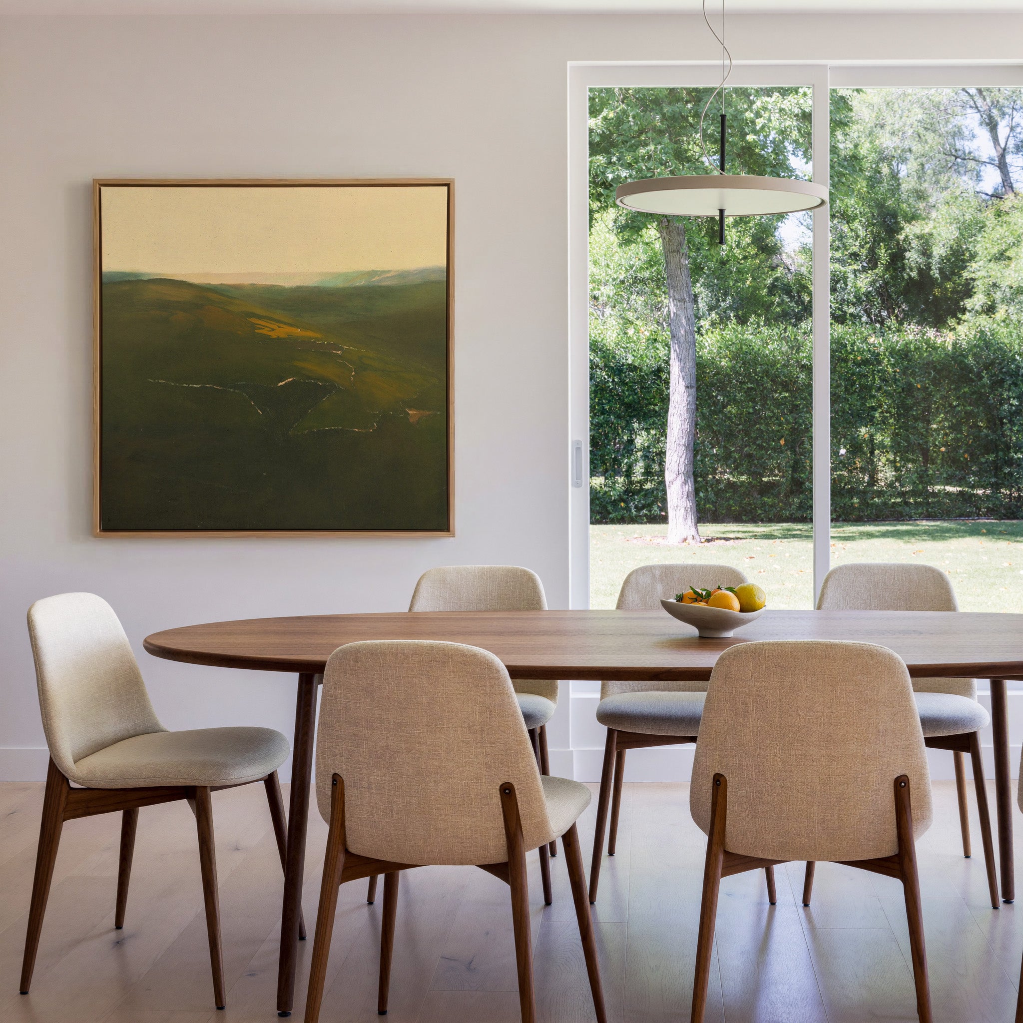 green valley landscape with a winding river and canvas wall art in an oak frame in a dining room