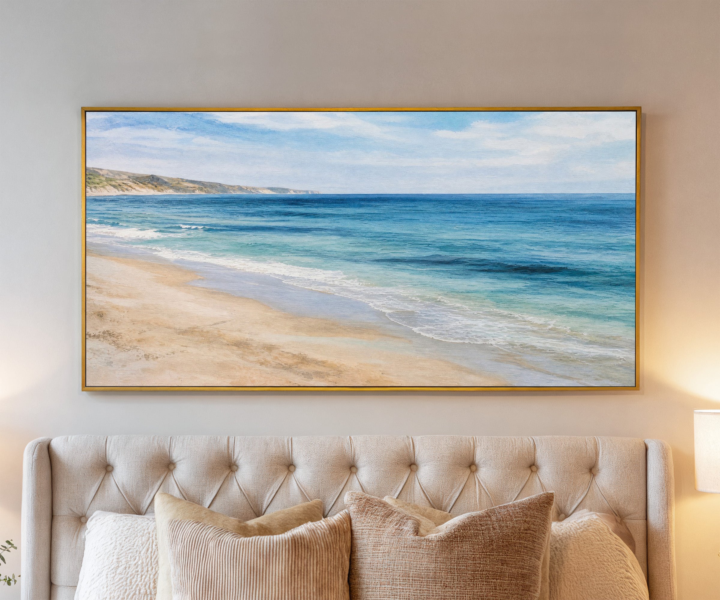 blue sea with pale sand and distant headland canvas wall art in a gold frame above a bed