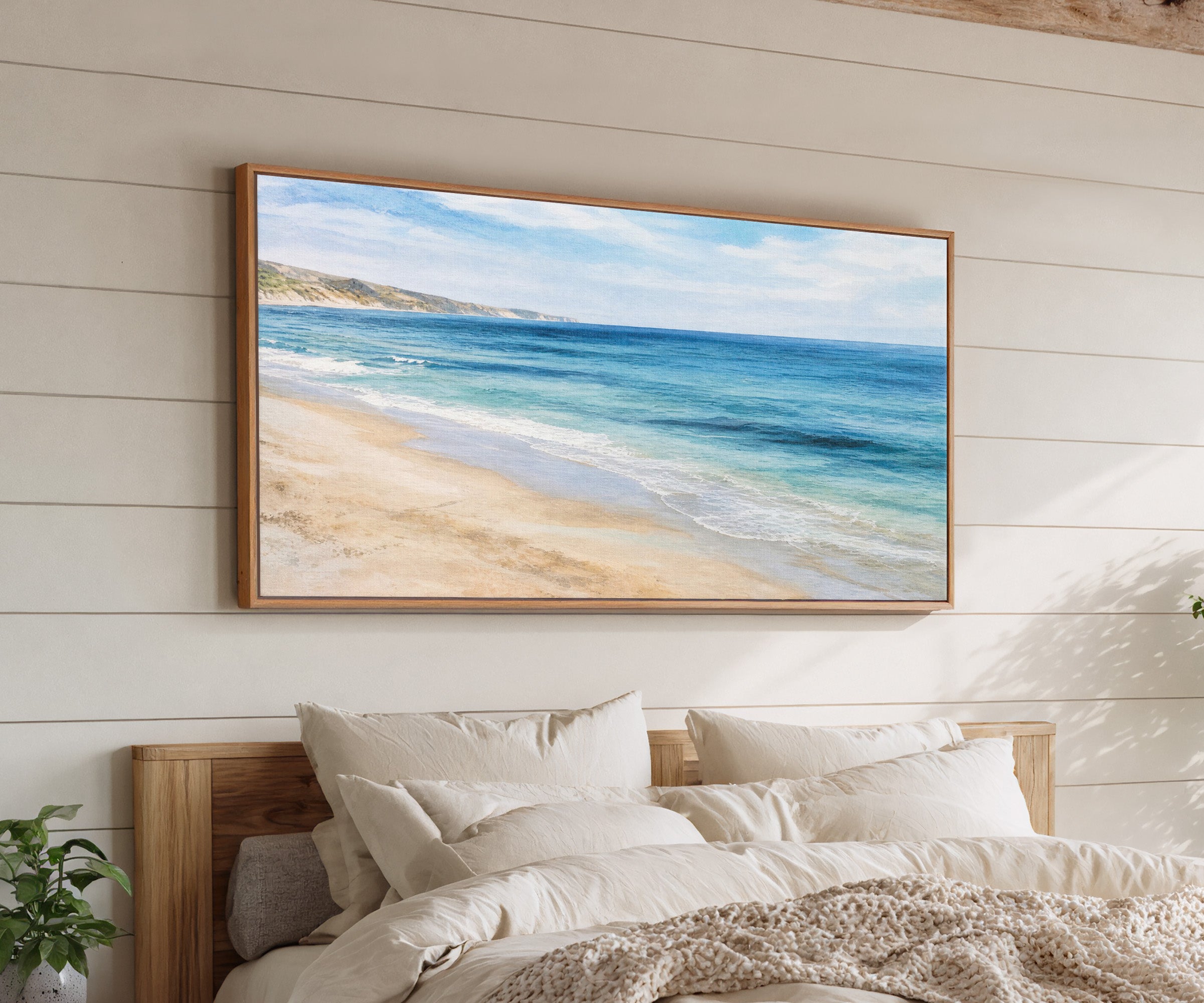 blue sea with pale sand and distant headland canvas wall art in an oak frame above a bed