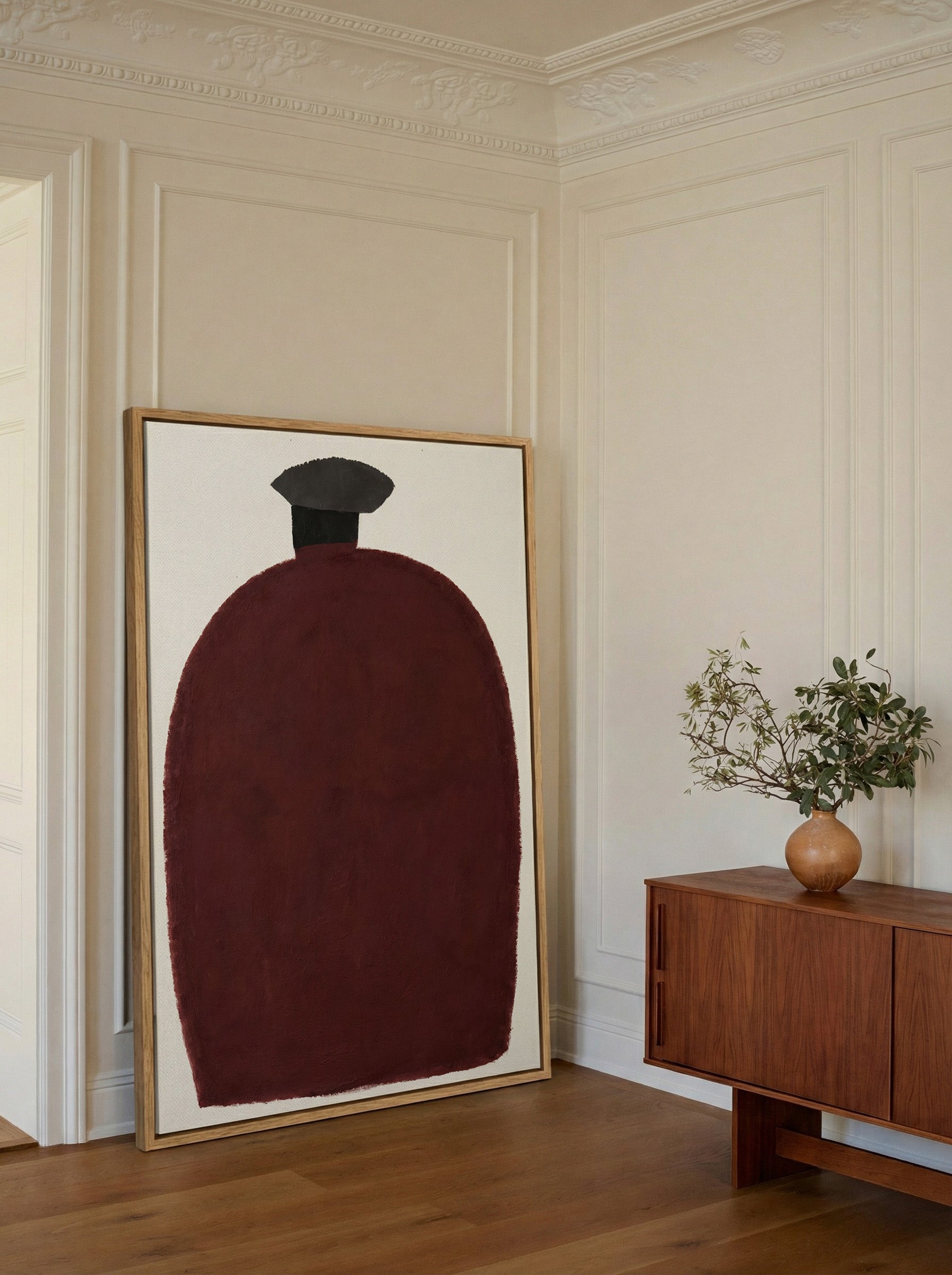 deep burgundy vessel shape with a dark cap on canvas wall art in an oak frame in a styled room setting