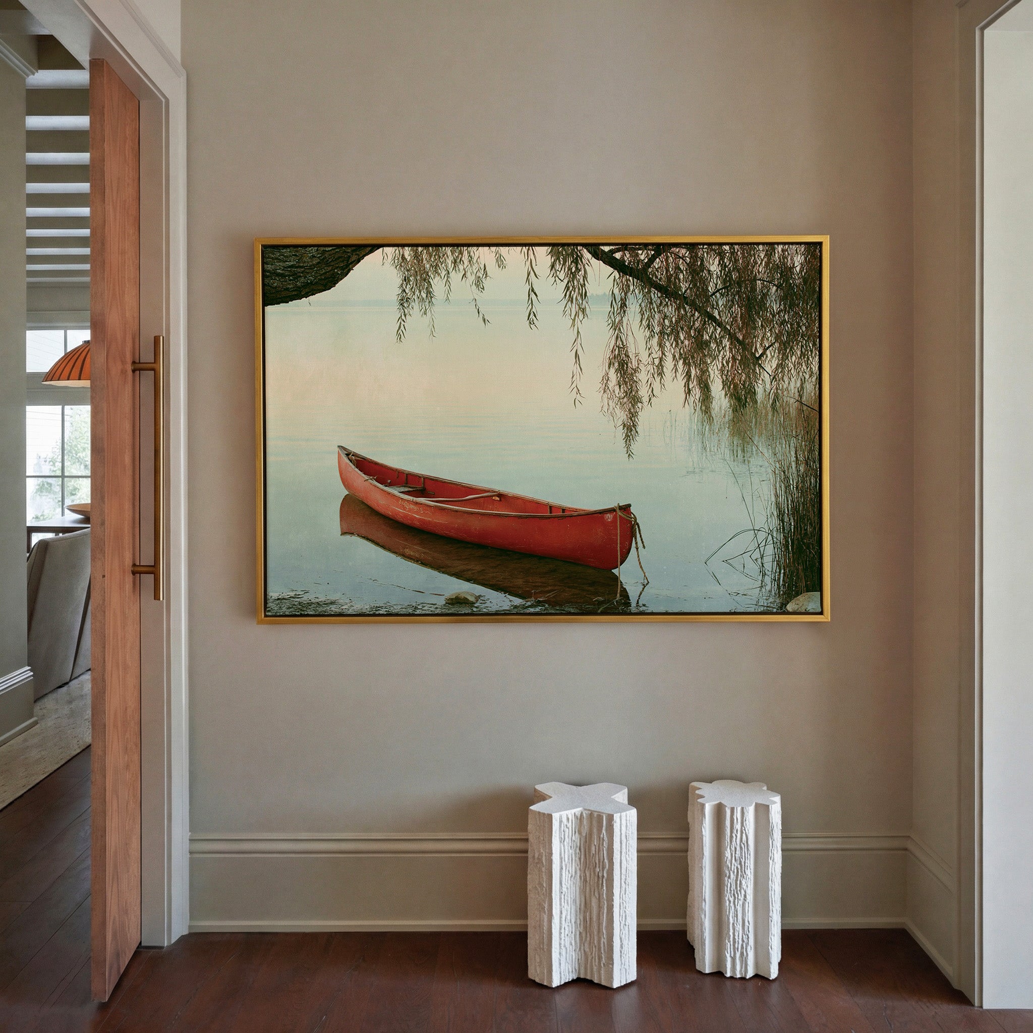 red canoe under hanging willow branches by canvas wall art in a gold frame in a styled room setting