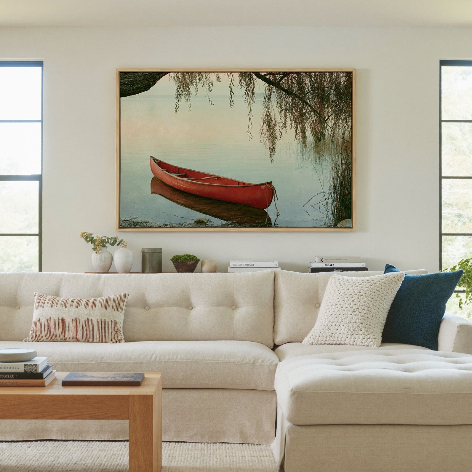 red canoe under hanging willow branches by canvas wall art in a natural wood frame in a living room