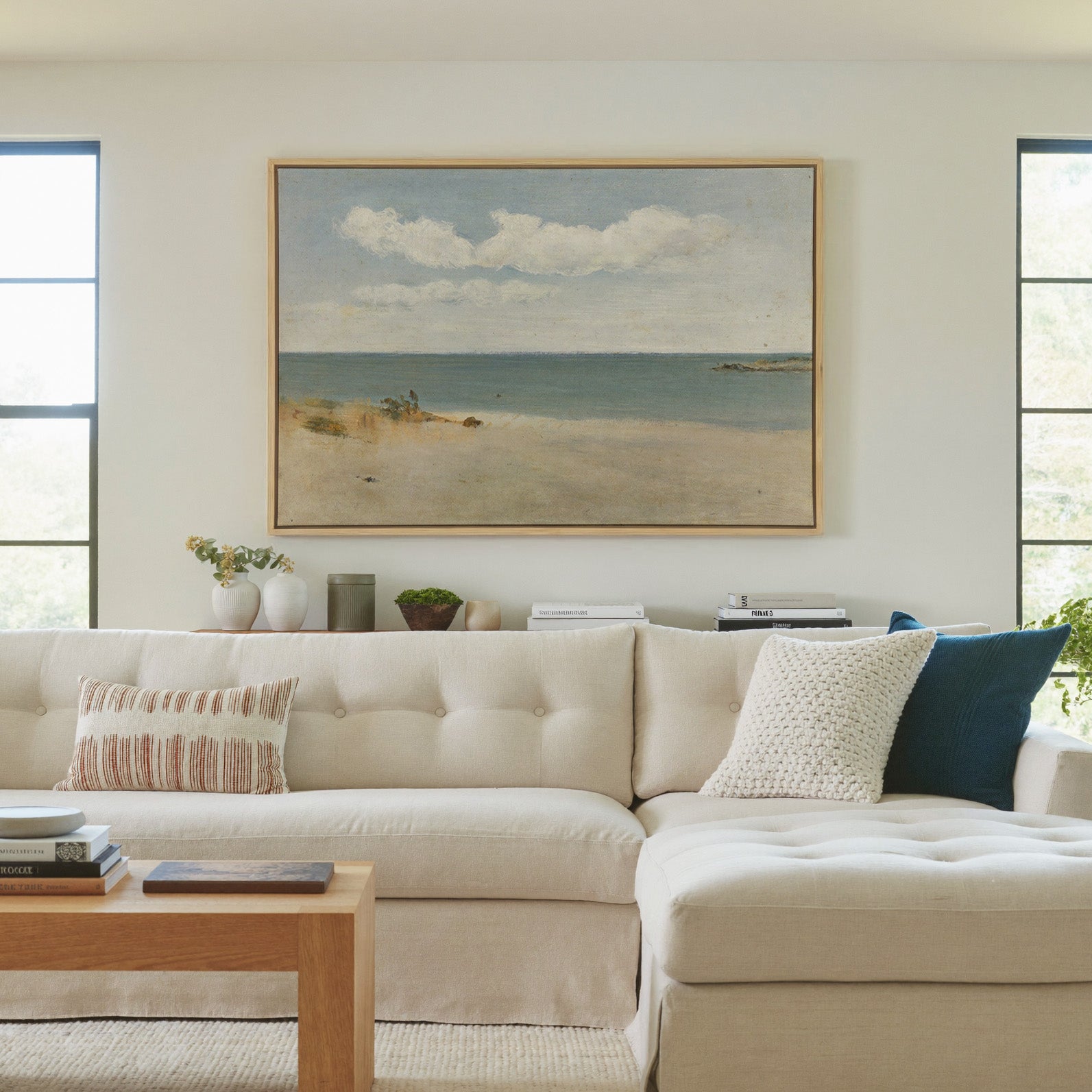 pale beach, blue green water, and broad white canvas wall art in a natural wood frame in a living room