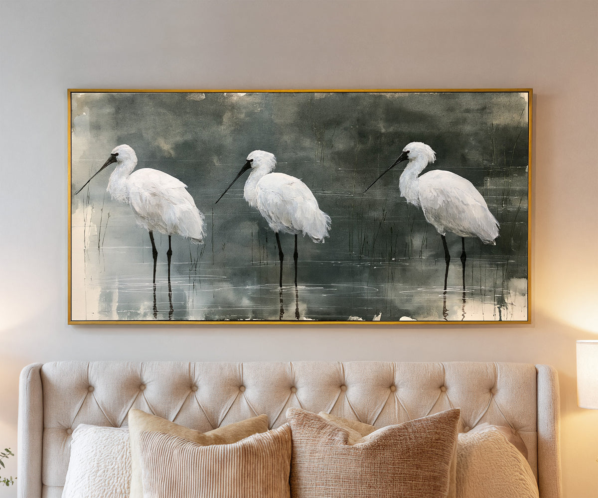 three white birds in shallow marsh water canvas wall art in a gold frame above a bed
