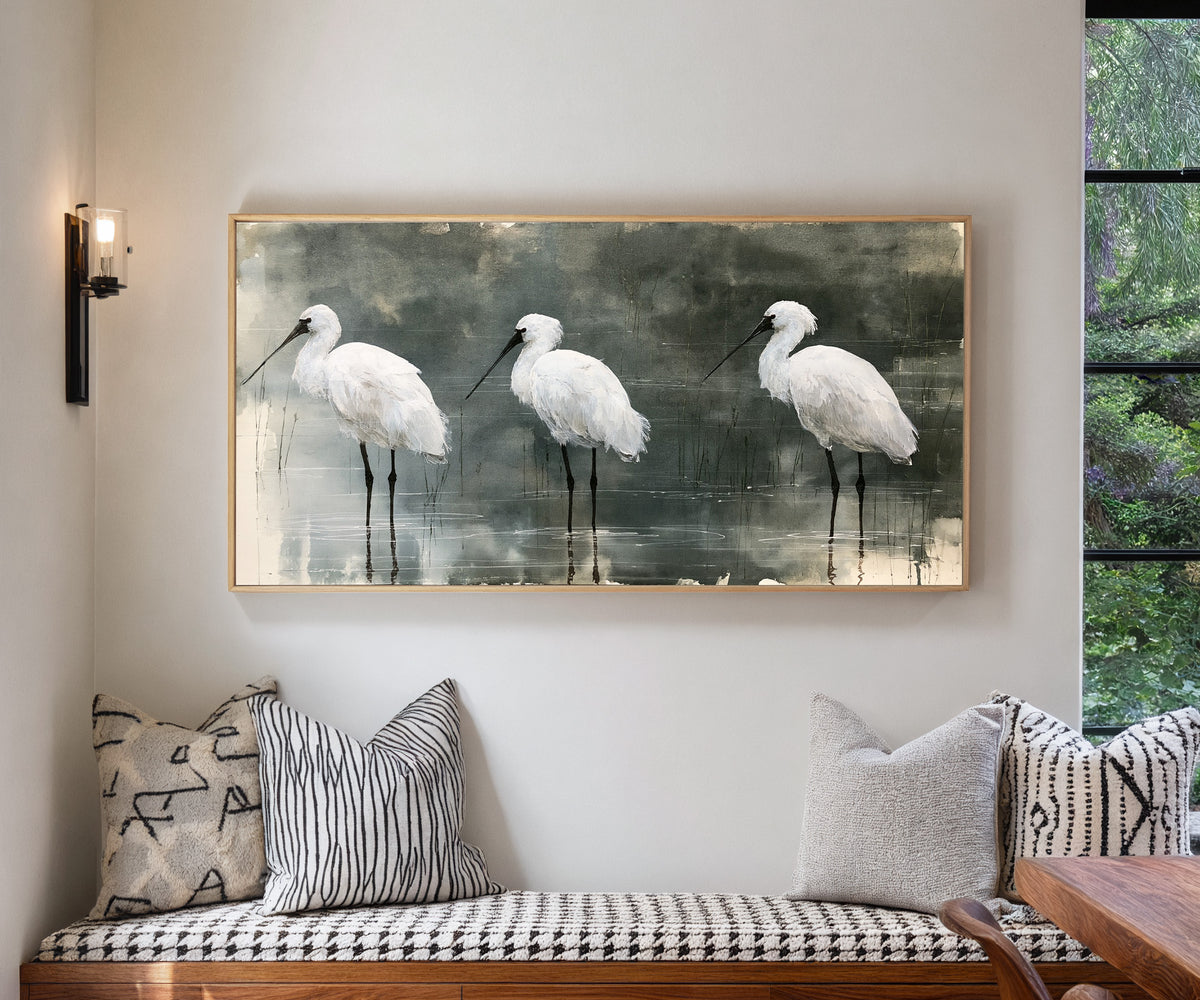 three white birds in shallow marsh water canvas wall art in a natural wood frame in a living room
