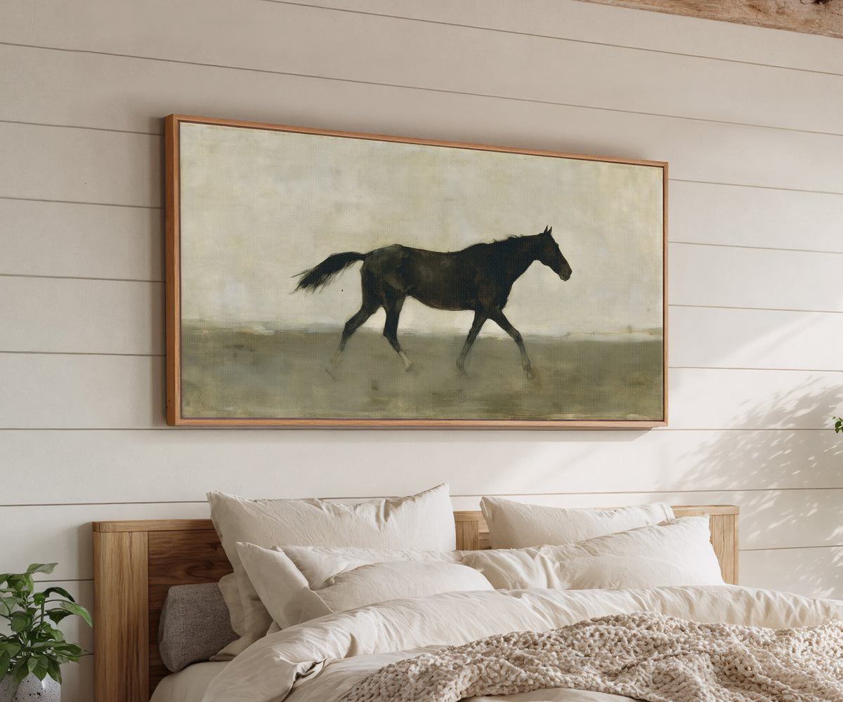 single dark horse in a pale open field canvas wall art in an oak frame above a bed
