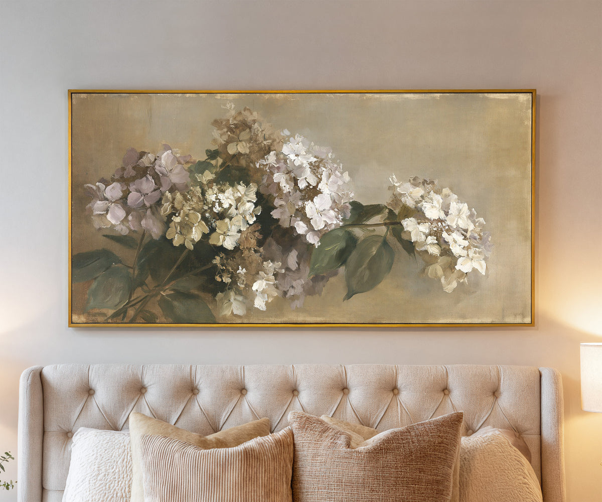 faded hydrangea cluster in cream, mauve, and canvas wall art in a gold frame above a bed
