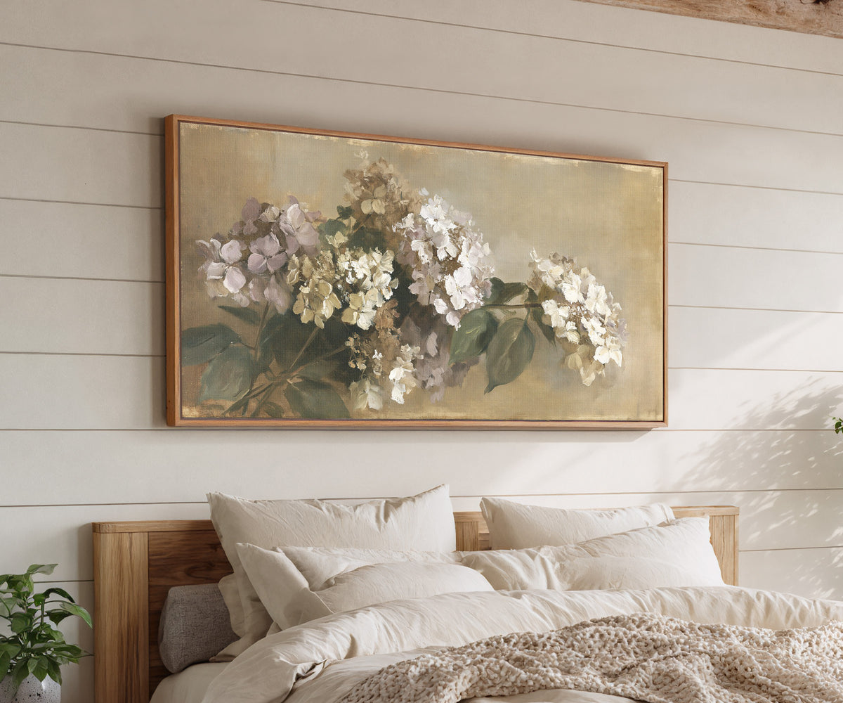 faded hydrangea cluster in cream, mauve, and canvas wall art in an oak frame above a bed