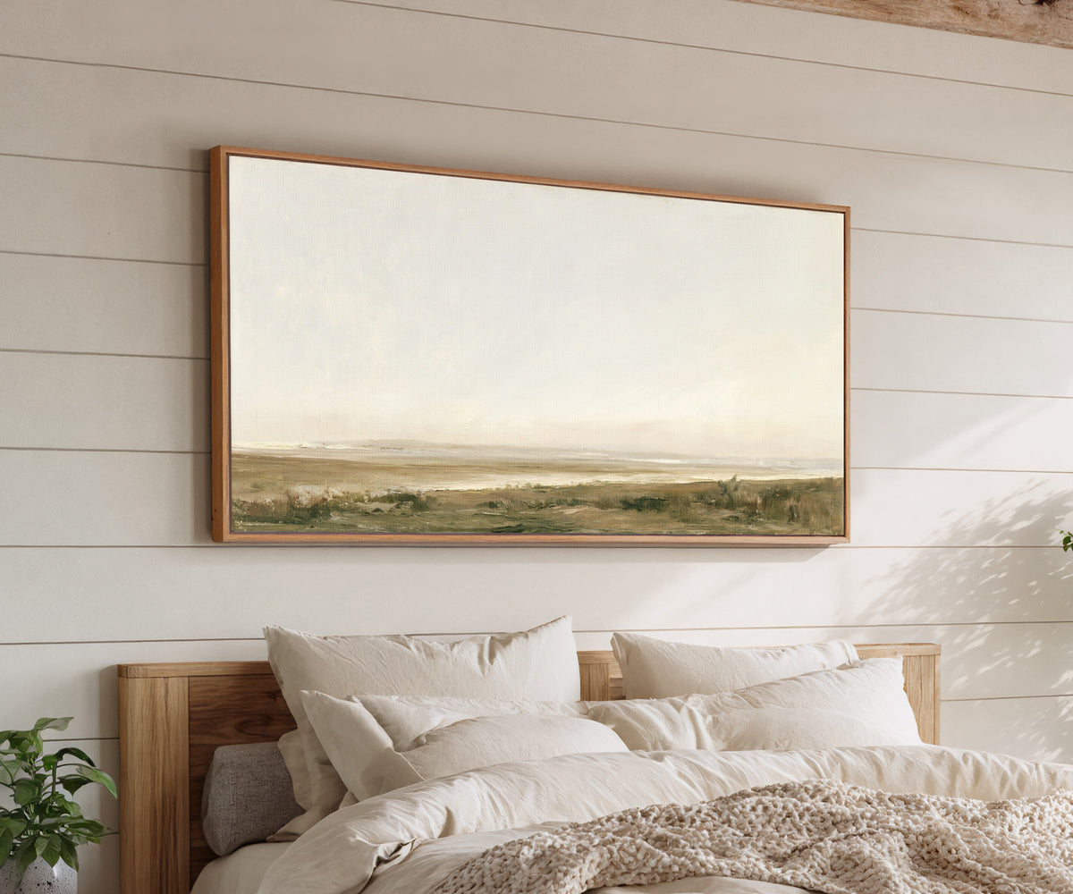 pale coastal landscape with low marshy ground canvas wall art in an oak frame above a bed