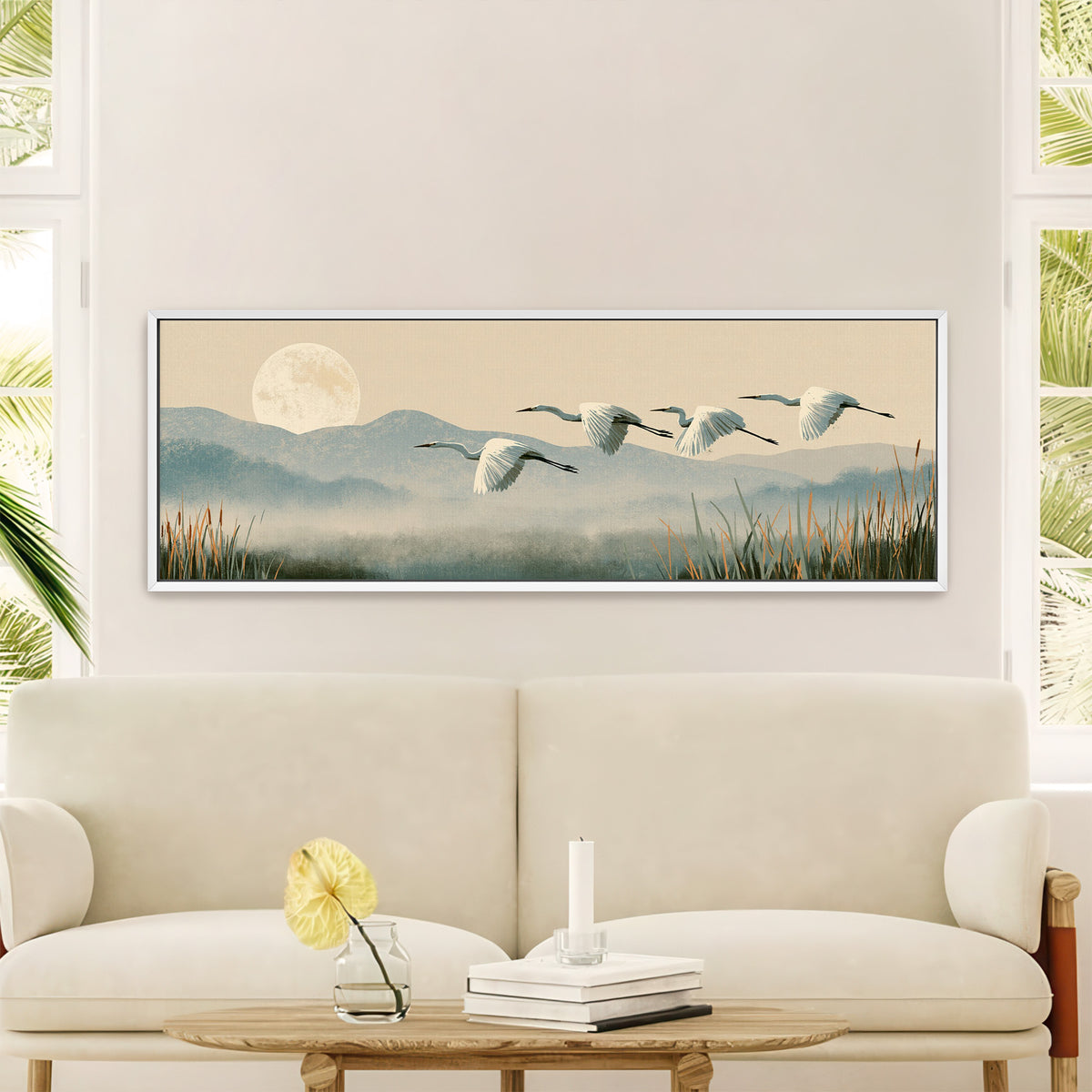 four white egrets flying above canvas wall art in a white floater frame in a styled room setting