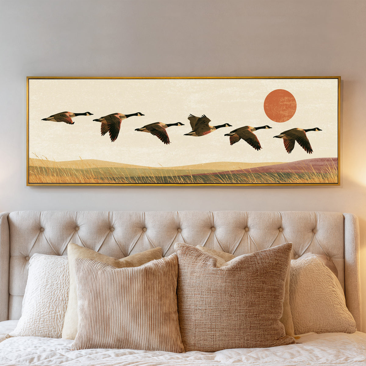 six canada geese flying over golden grass canvas wall art in a gold floater frame above a bed