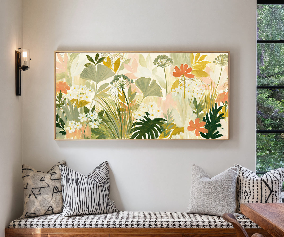 white daisies and coral flowers among layered canvas wall art in a natural floater frame in a living room
