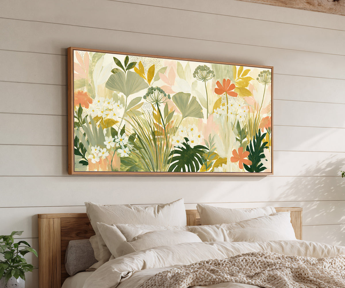 white daisies and coral flowers among layered canvas wall art in an oak finish floater frame above a bed