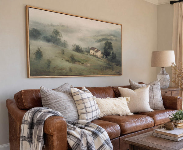 This horizontal canvas wall art features a hazy, pastoral landscape with two white houses nestled on a rolling green hill, rendered in a soft, muted palette. It hangs above a.