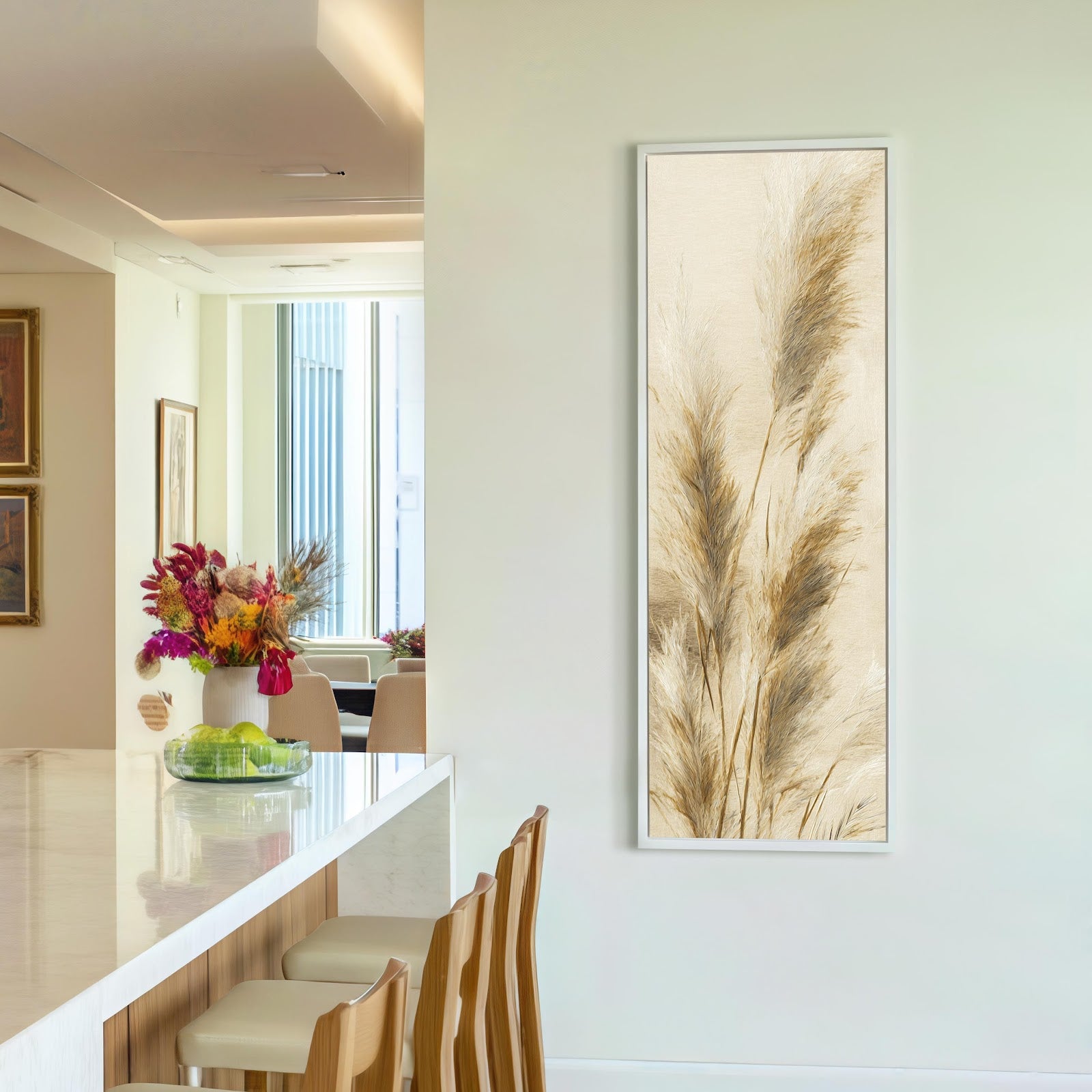 This vertical painterly print of feathery pampas grass in neutral tones is displayed in a white floater frame on an off-white wall beside a marble-topped kitchen bar.