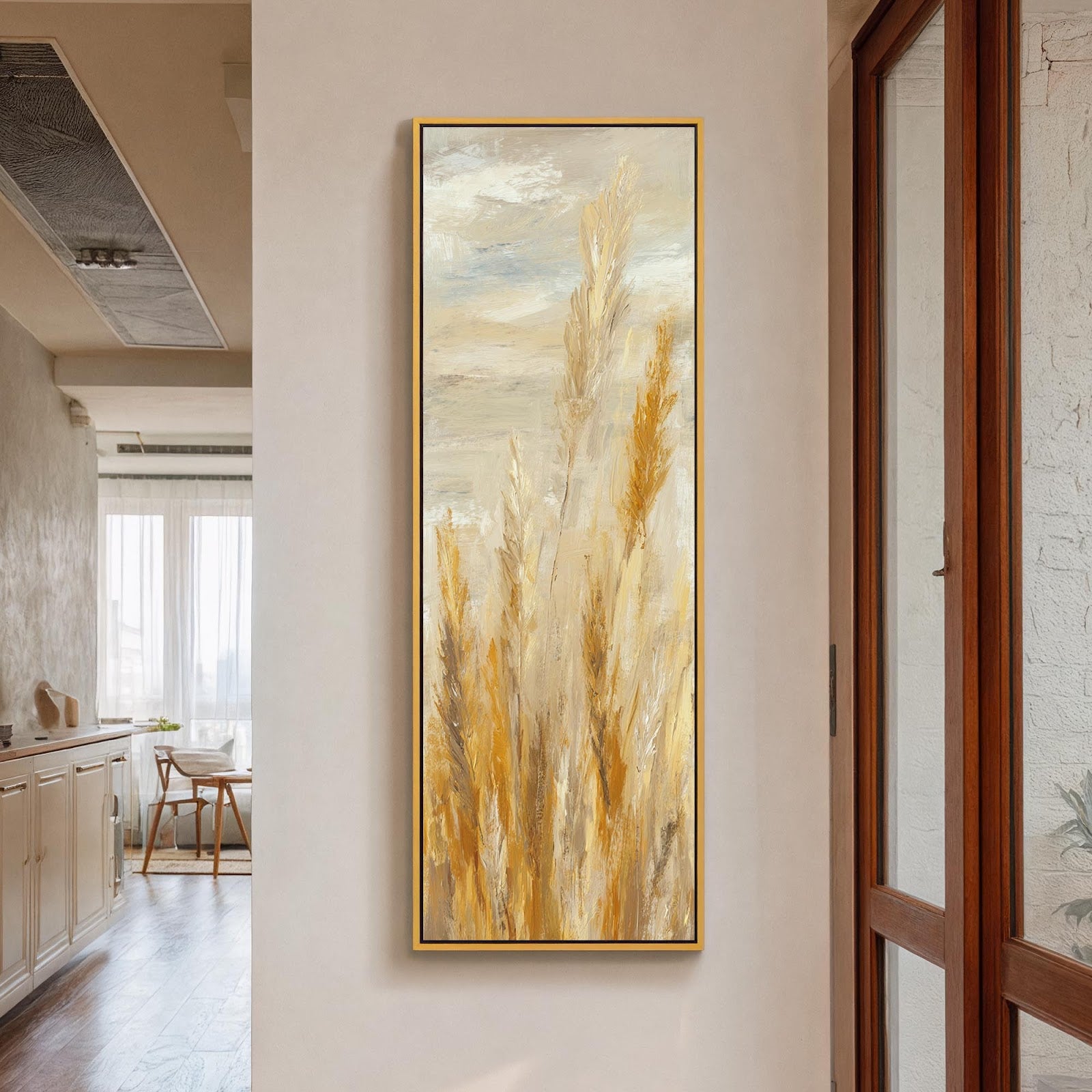 This vertical canvas art print features textured golden pampas grass in an impressionistic style, mounted in a gold floater frame on a beige hallway wall beside a wooden door.