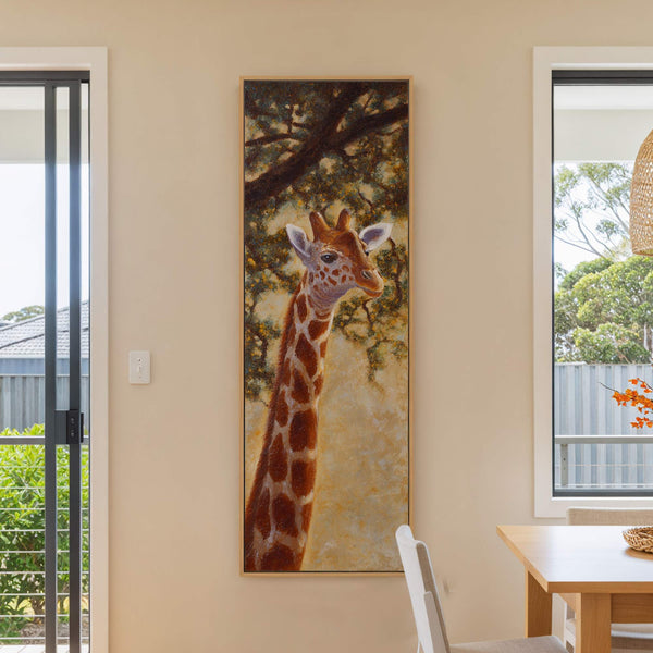 A vertical, nature-inspired canvas print shows a giraffe in a textured, warm-toned palette against a background of lush foliage and tree branches, framed by a natural wood floater frame, hanging.
