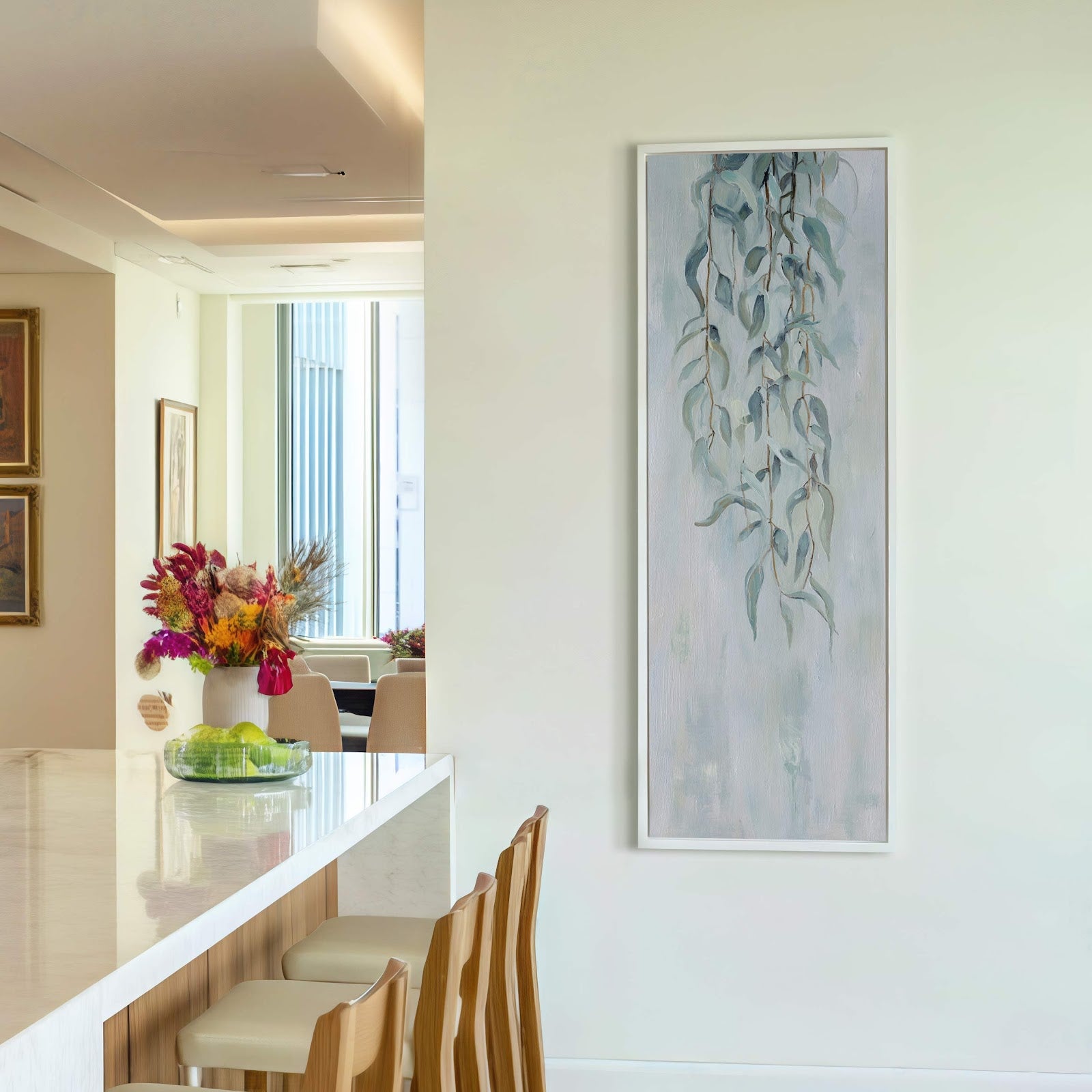This vertical canvas print features a soft, painterly style with a muted green and blue palette depicting delicate eucalyptus leaves. It is framed in white and hangs on a neutral.
