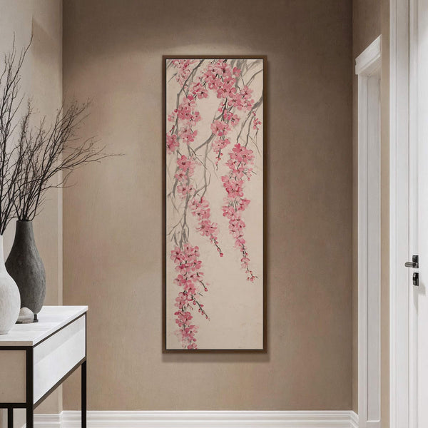 This vertical canvas wall art features a traditional-style painting of pink cherry blossoms cascading from grey branches on a neutral palette. It is displayed on a tan wall next to.