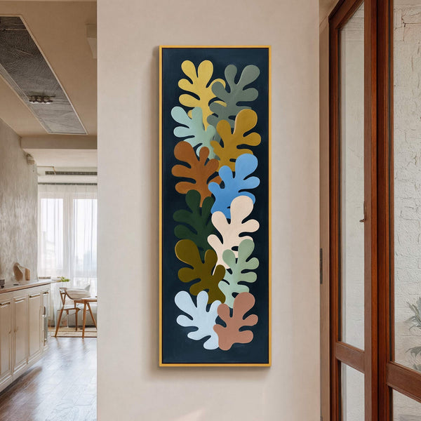 This vertical, abstract art print features a collage of organic shapes in a palette of mustard yellow, sage green, rust brown, and sky blue against a dark background, framed in.