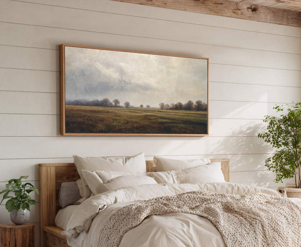 A horizontal canvas print of a cloudy, atmospheric landscape painting with muted greens and browns hangs above a bed on a white shiplap wall.