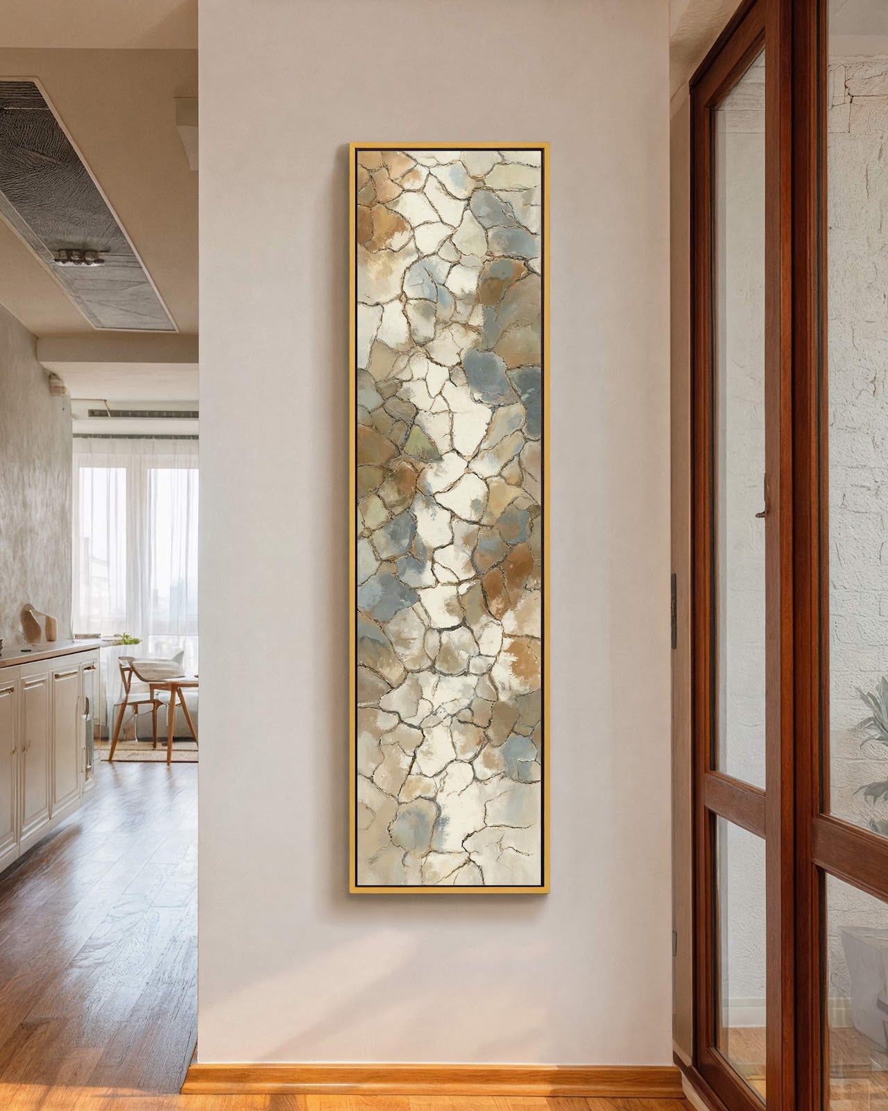 This vertical canvas print features an abstract mosaic of earth tones and blue in a gold floater frame on a white hallway wall near a wooden glass door.