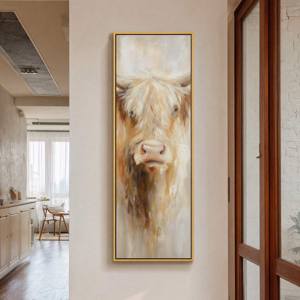 This vertical, oil-style painting print features a close-up portrait of a Highland cow with a warm, earthy palette, framed in gold, and displayed on a light neutral wall in a.