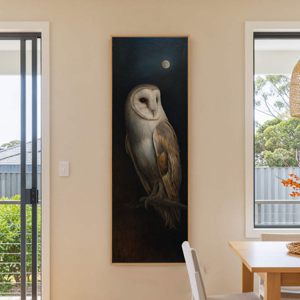 This vertical art print features a realistic barn owl with a dark, moonlit background and a neutral palette. It is set in a room with cream walls and a wooden.