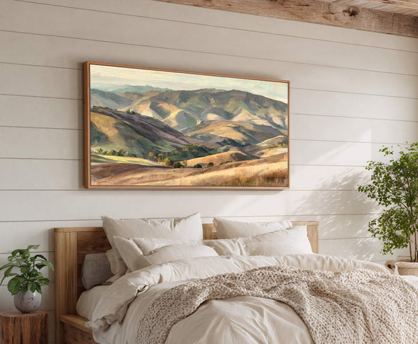 A horizontal canvas wall art depicts rolling hills in a painterly style with a warm, earthy palette, displayed in a bedroom with white paneled walls and a wooden bed frame.