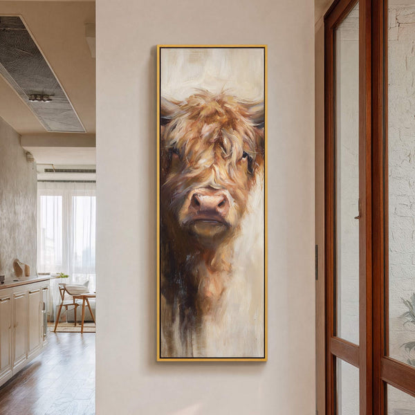 This vertical art print features a textured, painterly close-up of a Highland cow with a warm, earthy palette, framed in gold and displayed on a neutral wall.