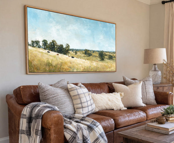 This horizontal landscape painting print features a pastoral scene with cows grazing in golden fields under a bright blue sky, rendered in an impressionistic style. It is displayed on a.