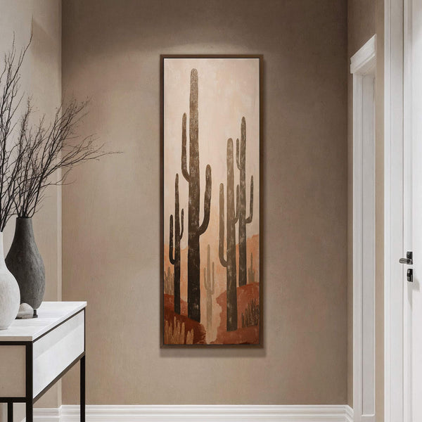 This vertical canvas wall art displays saguaro cacti in a desert landscape using a warm, earthy palette and a stylized, minimalist art style. It is framed in a natural wood.