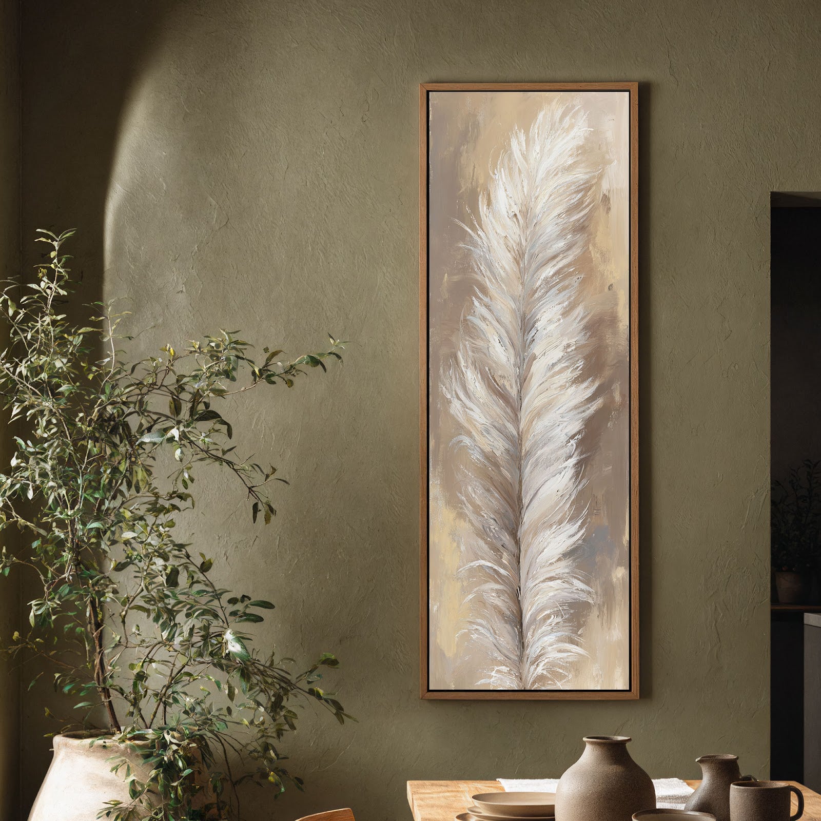 This vertical canvas print showcases a painterly white feather in neutral tones, set in an oak floater frame on a textured olive living room wall beside a large plant.