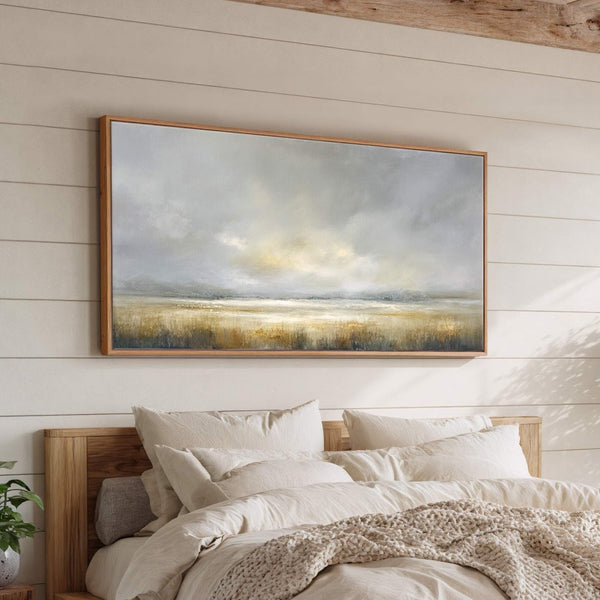 This horizontal canvas wall art features an abstract landscape painting with a muted palette of grays, yellows, and greens, framed in natural wood, displayed above a bed with neutral linens.